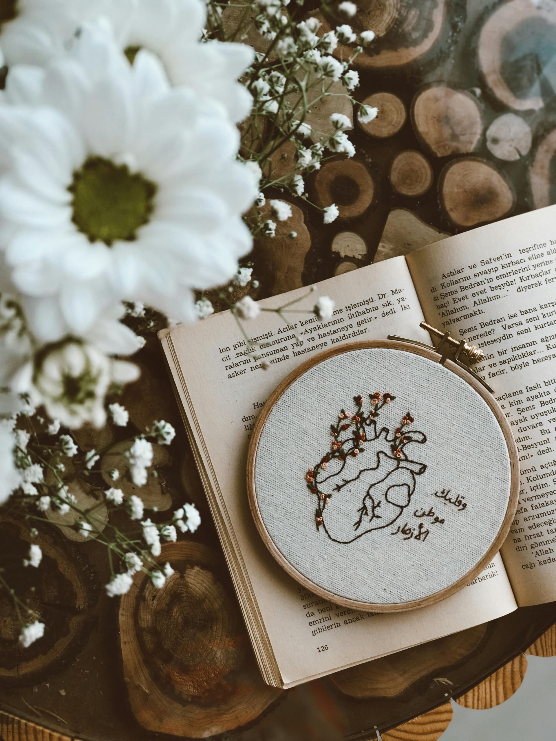A beautiful floral embroidery hoop displayed on an open book surrounded by daisies and baby's breath.
